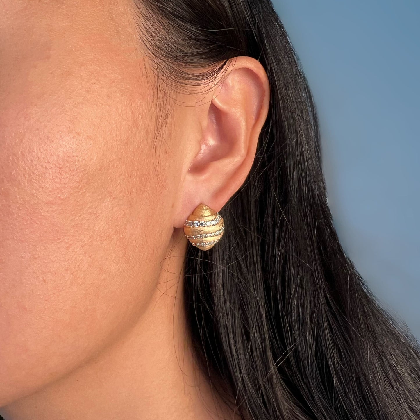 Model showcasing an elegant croissant-shaped golden silver earring adorned with simulated diamonds, with the metal surface treated to have a velvety texture.