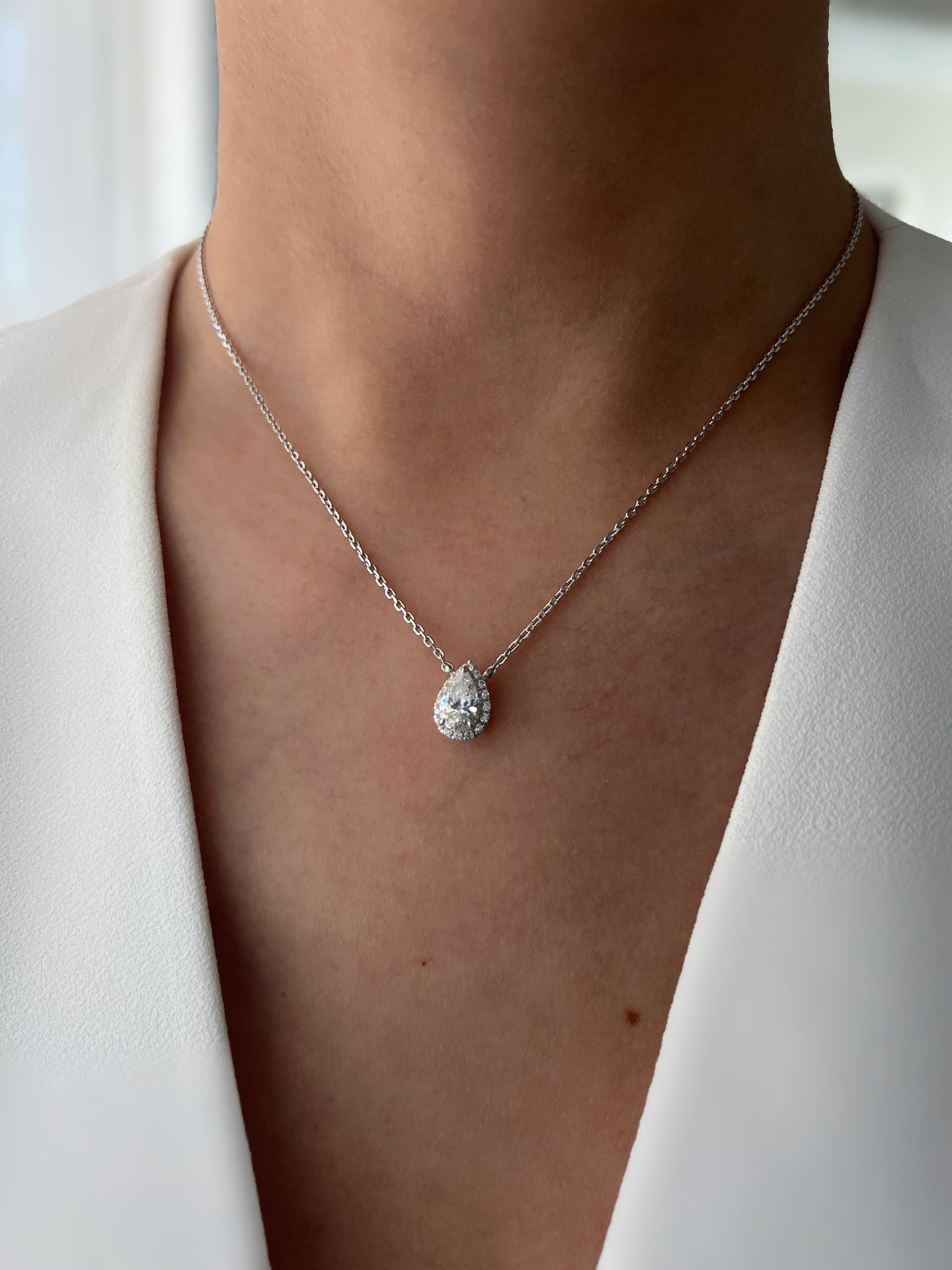 Model showcasing a 1.5 carat pear-shaped cubic zirconia pendant necklace with hidden halo setting, highlighting the necklace's brilliance and its delicate placement around the neck.