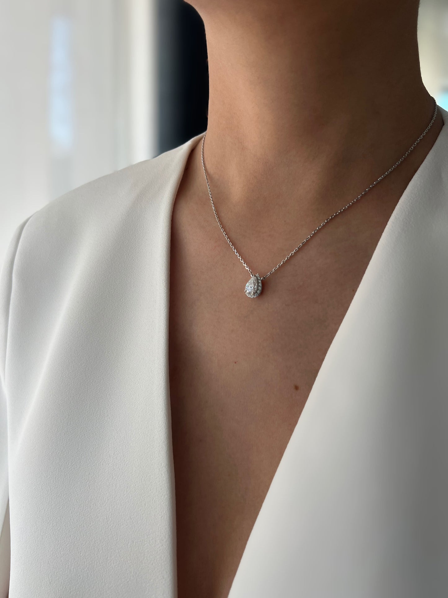 Side view of a model wearing a 1.5 carat pear-shaped cubic zirconia pendant necklace with hidden halo setting, highlighting the necklace's sparkle and delicate chain.