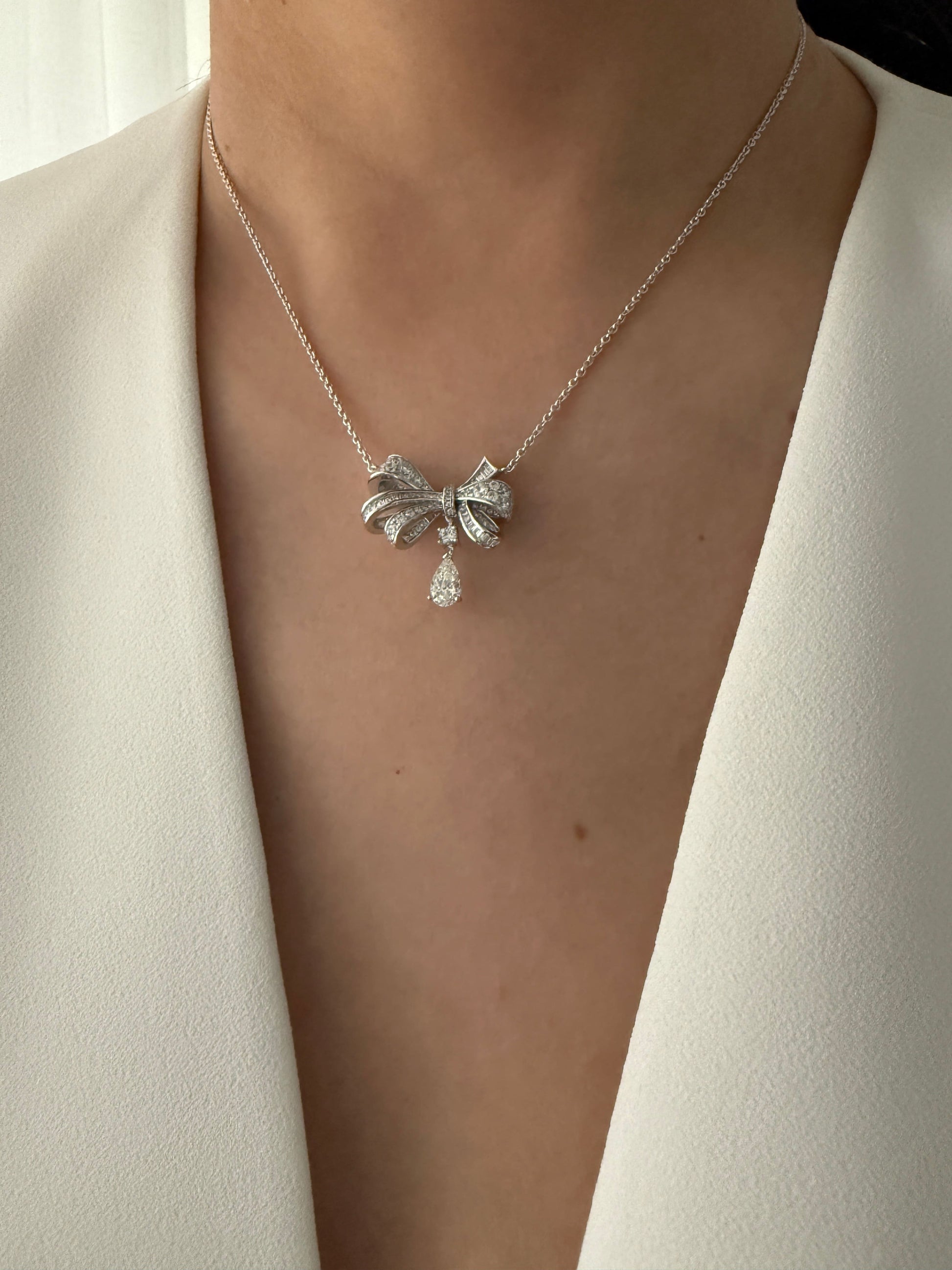 A model wearing the Belle Bow Necklace in silver, styled with a minimalist outfit for a chic look.